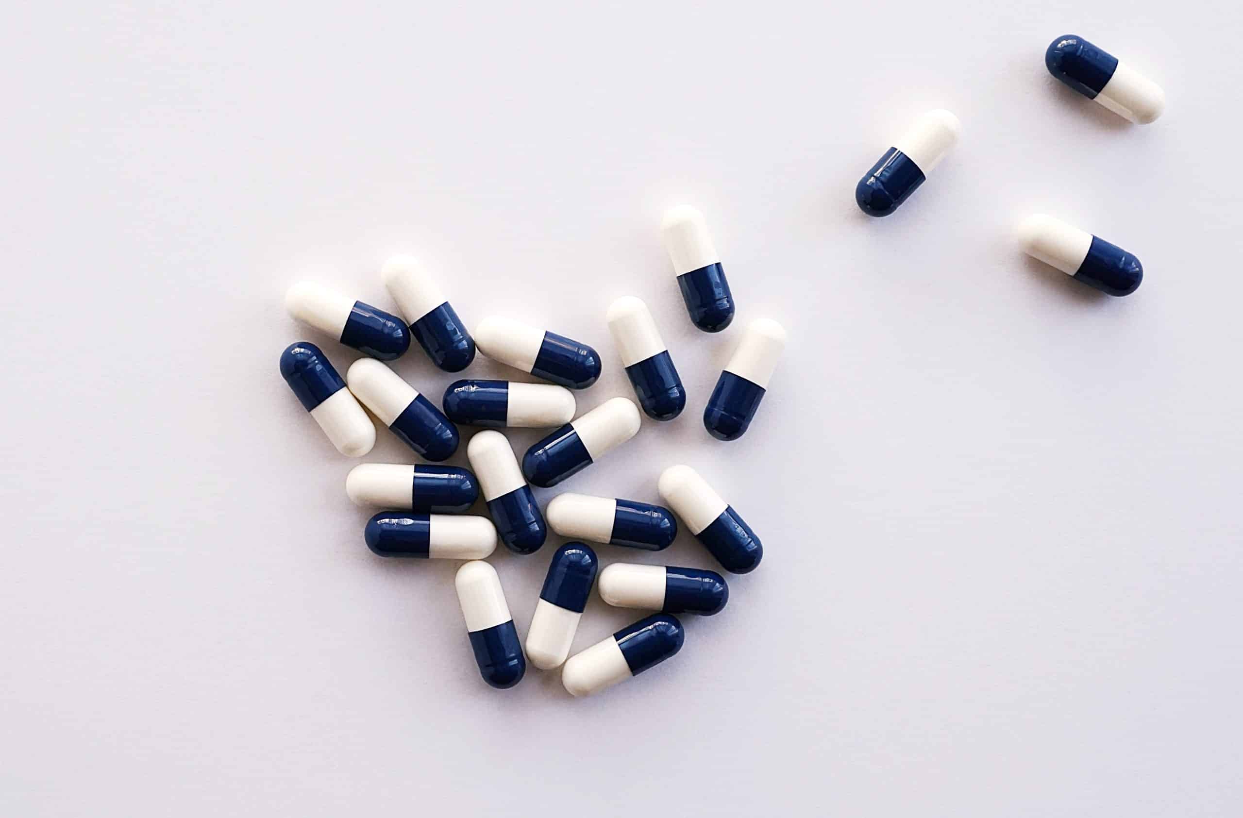 Canva-White-and-Blue-Medication-Pills-scaled Pile of blue and white pills on a white background